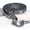 Stacks of multiple colorful custom Jacquard Webbing Tape rolls in different widths (30mm, 40mm) and designs including navy/gold and olive/black on a light grey fabric surface.